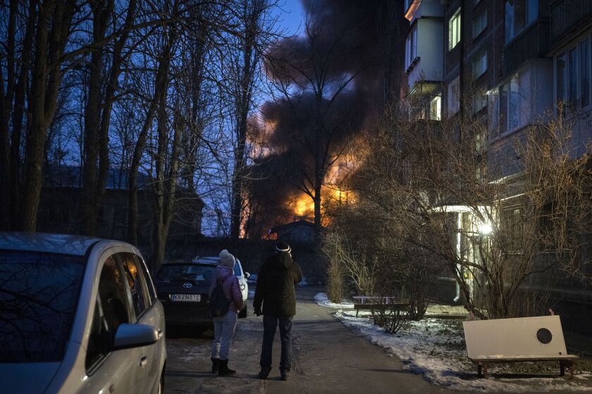 Residents watch at a burning infrastructure project hit during a massive Russian drone night strike in Kyiv, Ukraine, Monday, Dec. 19, 2022. (AP Photo/Efrem Lukatsky)