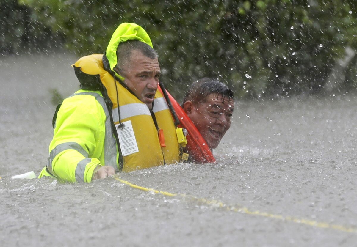 Wilford Martinez, right, is rescued from his flooded car by Richard Wagner of the Harris County Sheriff's Department along Interstate 610 on Sunday. (David J. Phillip / Associated Press)
