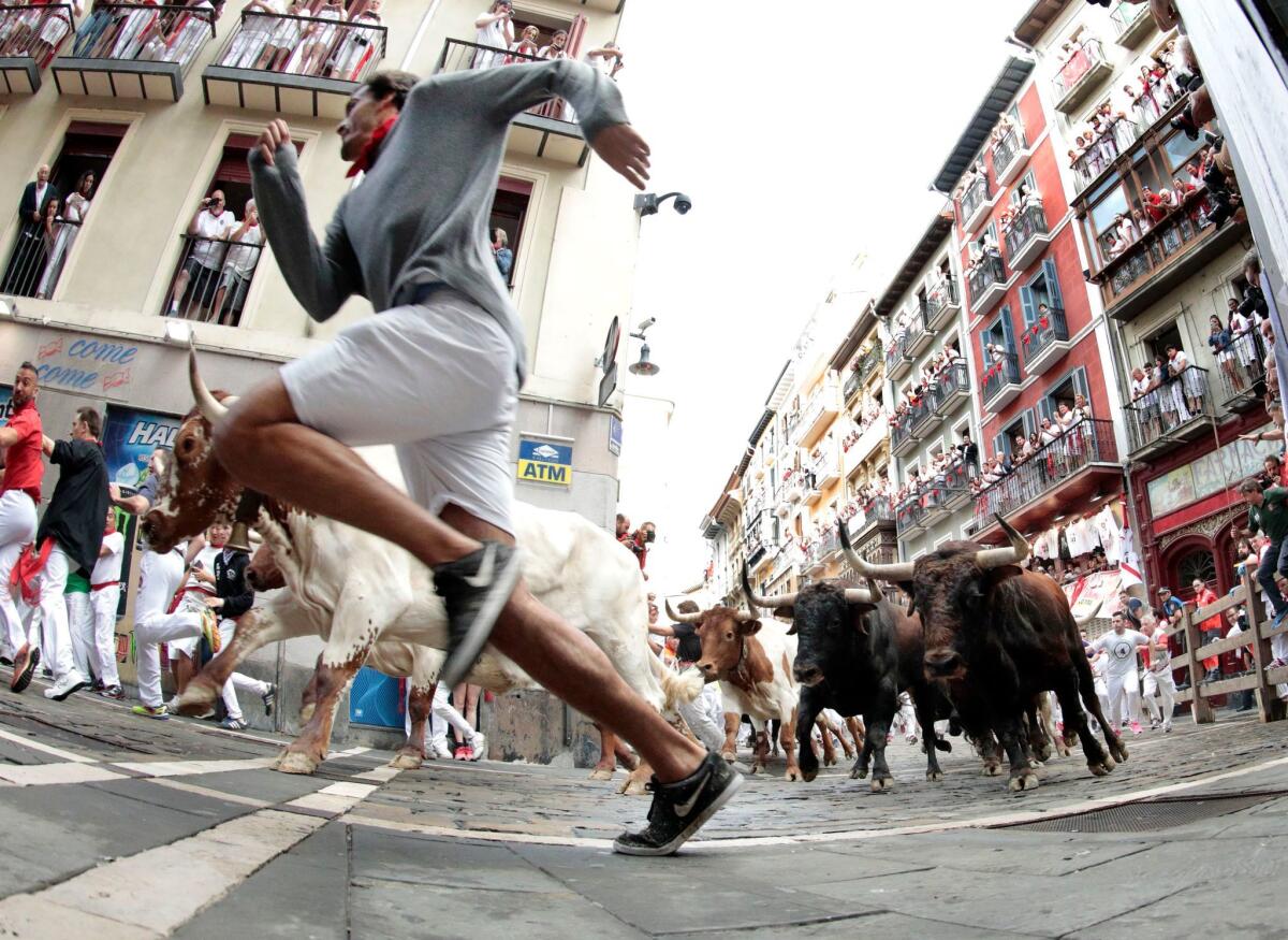 A runner in full stride leads a pack of bulls around a sharp curve in the old city streets of Pamplona. (Jim Hollander / EPA/Shutterstock)