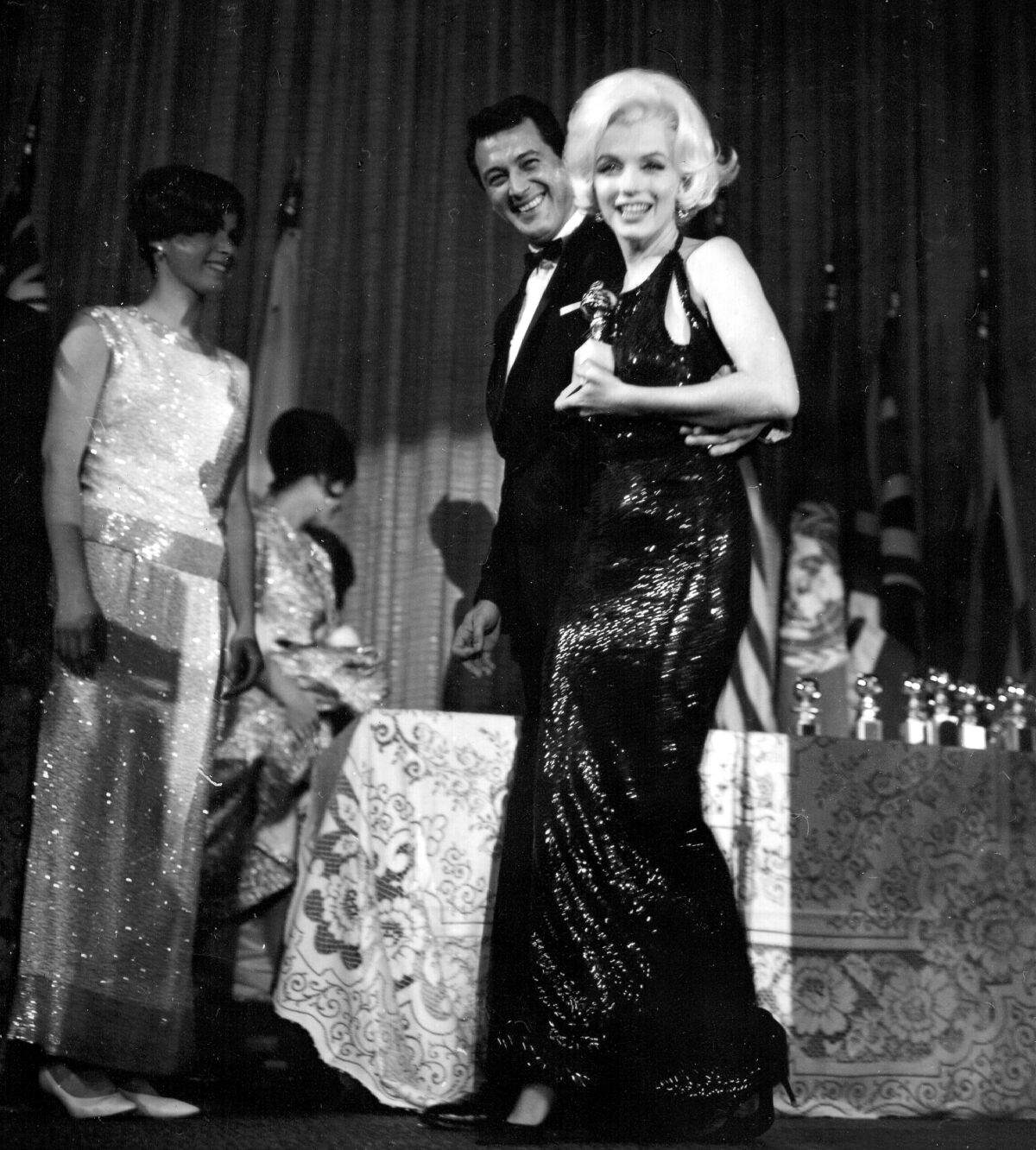 Marilyn Monroe in a long black evening gown holds a Golden Globe onstage.