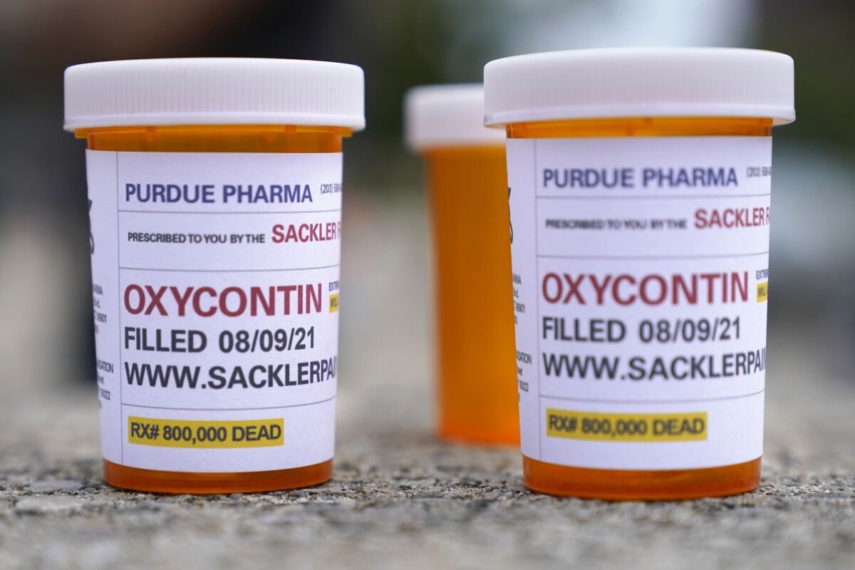 FILE - In this Aug. 9, 2021, file photo, fake pill bottles with messages about OxyContin maker Purdue Pharma are displayed during a protest outside the courthouse where the bankruptcy of the company is taking place in White Plains, N.Y. A federal judge on Wednesday, Oct. 13 allowed Purdue Pharma to resume its work carrying out the recent $10 billion settlement plan that allowed the Oxycontin maker to emerge from bankruptcy. (AP Photo/Seth Wenig, File)