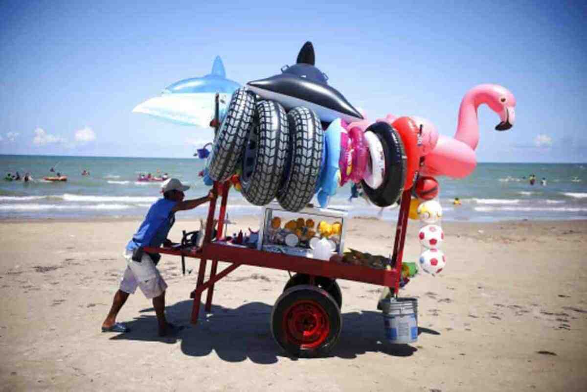 Un vendedor ambulante empuja un carrito con flotadores y vasos de fruta por la orilla de Playa Bagdad, cerca de la desembocadura del Río Bravo y de la ciudad fronteriza de Matamoros, México.