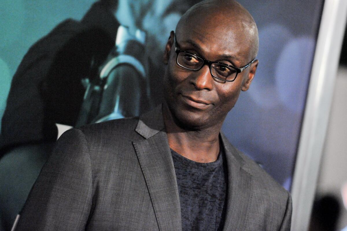 Lance Reddick in a suit looking to his right