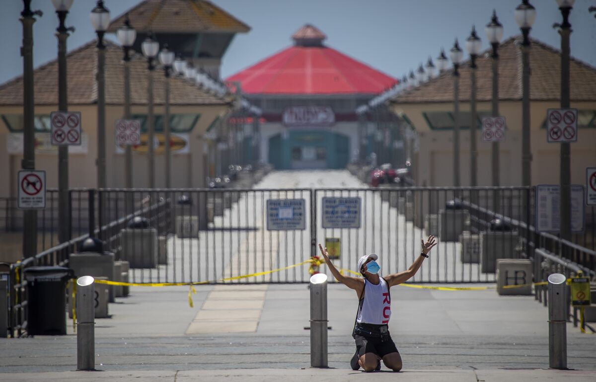Woman kneels in prayer in front of closed Huntington Beach Pier