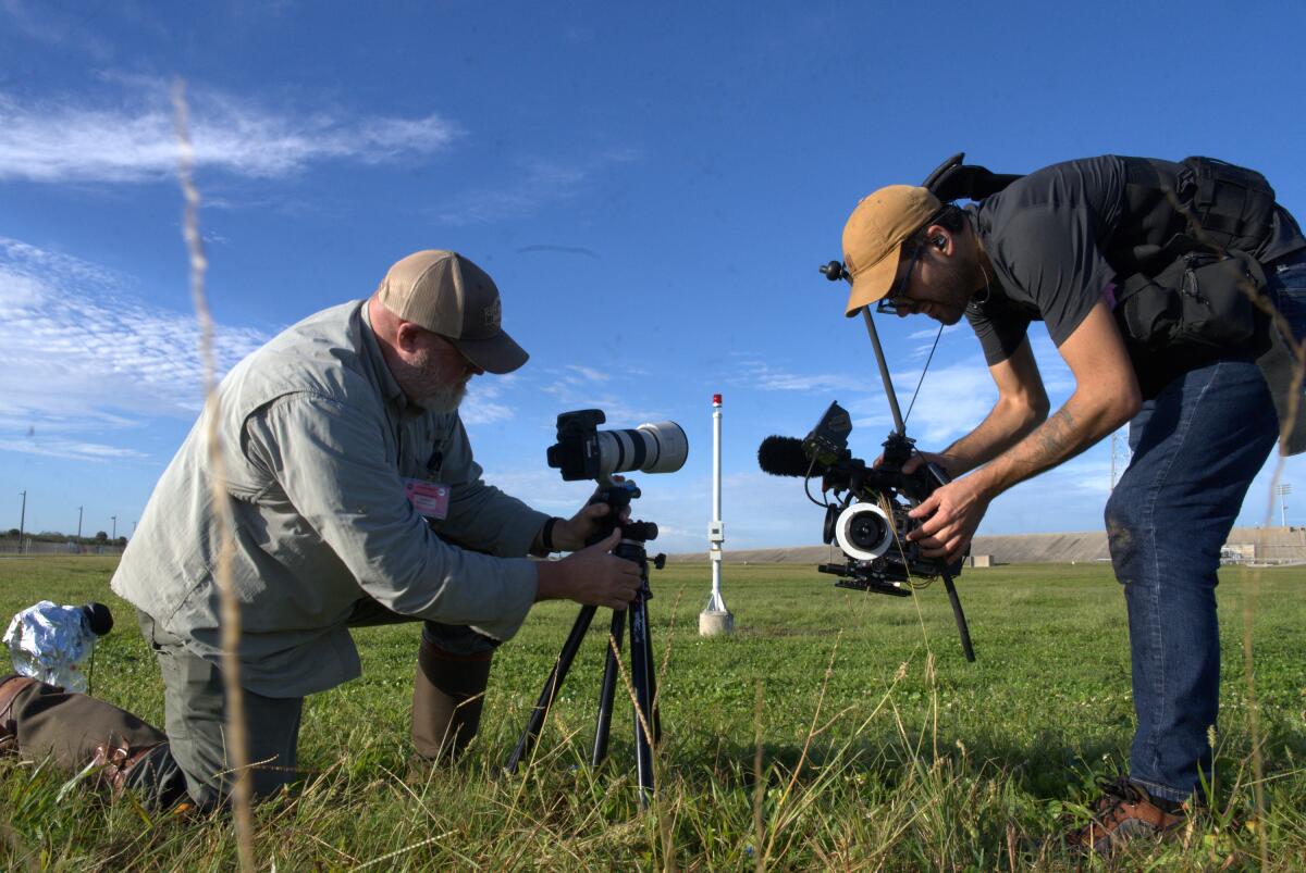 A man films another man taking a photograph in a field