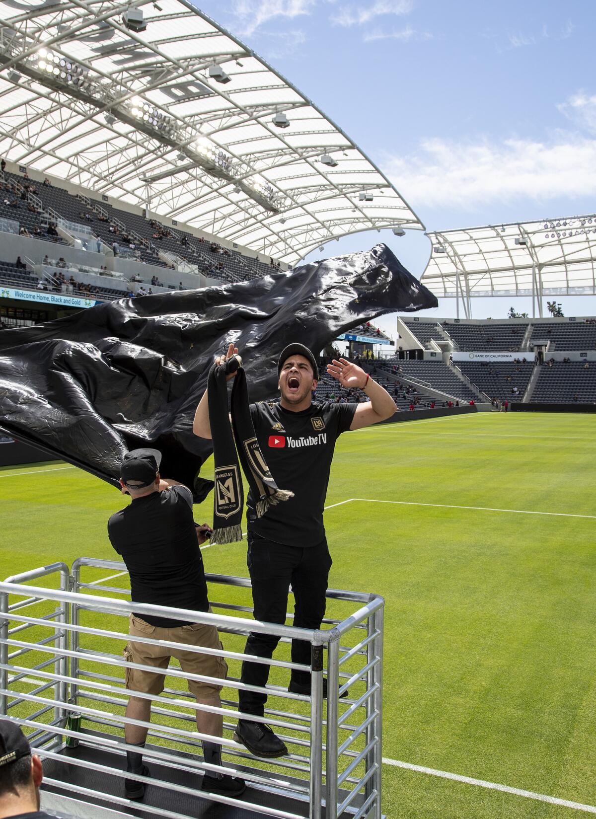 David Cordero of Victorville, right, leads a rally group called the Empire Boys while watching an LAFC soccer game on giant video screens inside the Banc of California Stadium.