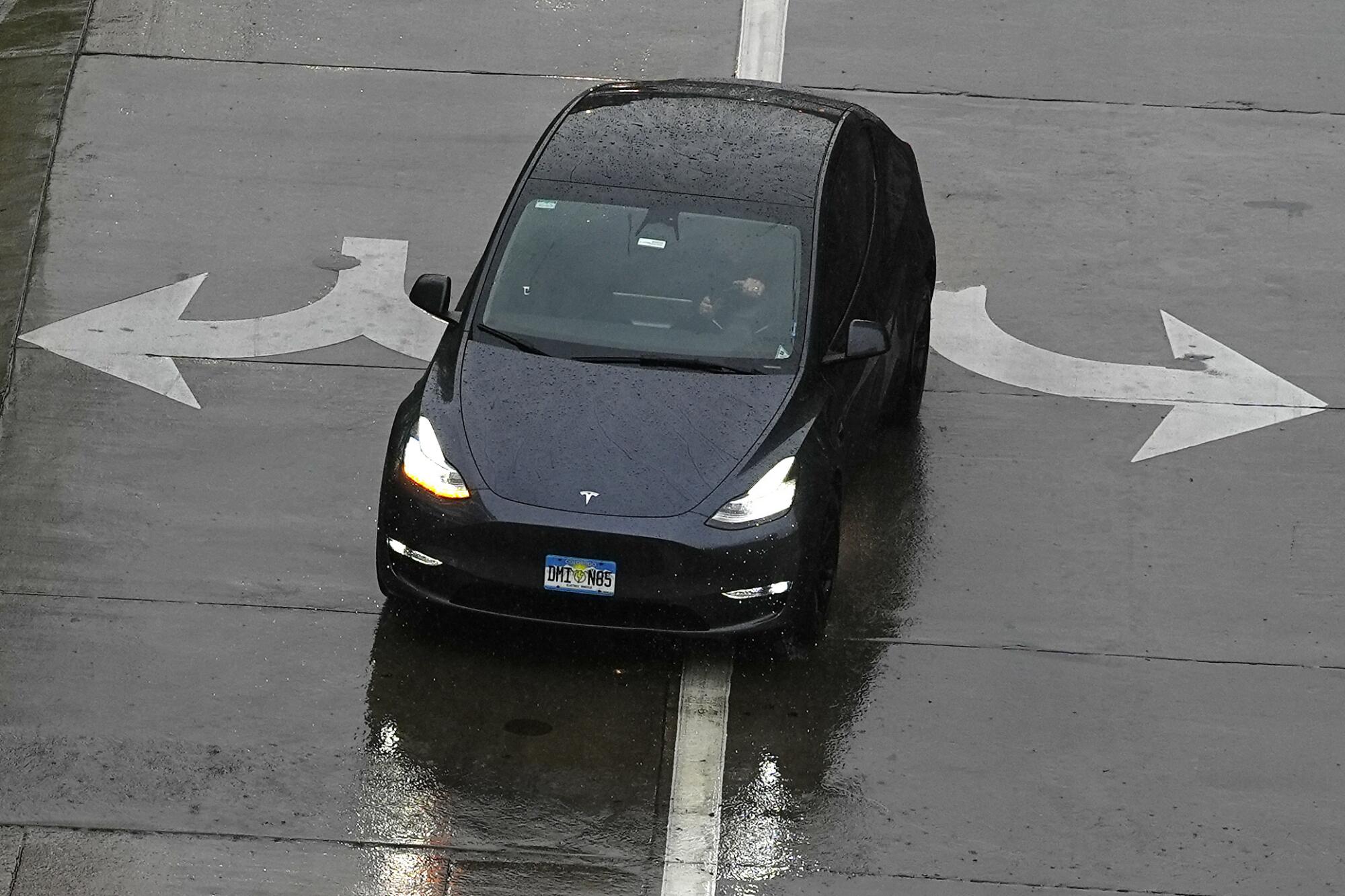 A black Tesla in the middle of a wet road with arrows pointing in opposite directions