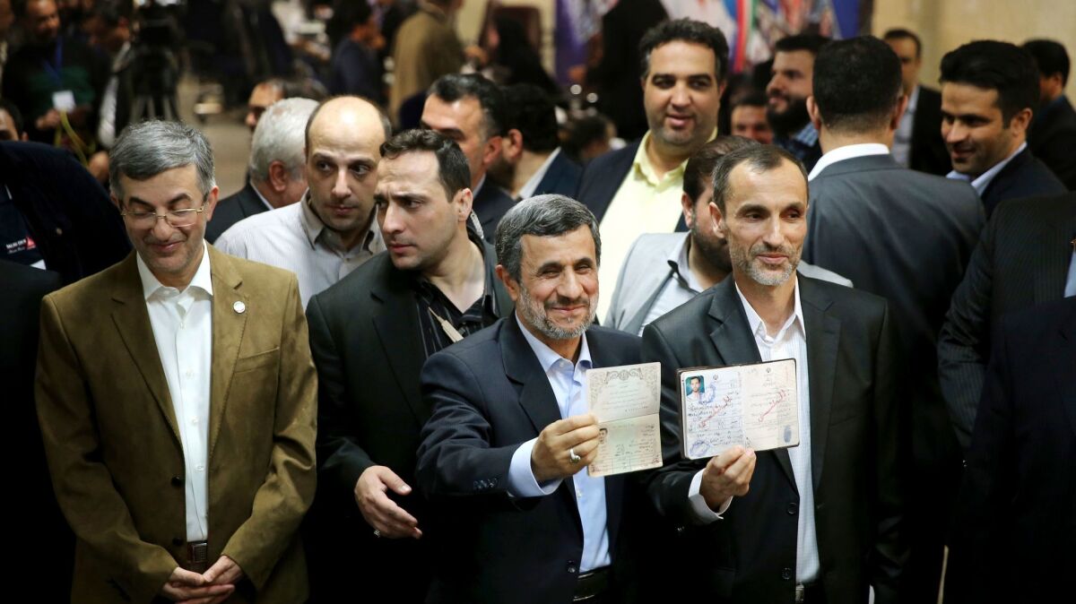 Former Iranian President Mahmoud Ahmadinejad, center, and ally Hamid Baghaei, right, show their identifications Apil 12 after registering for presidential elections.