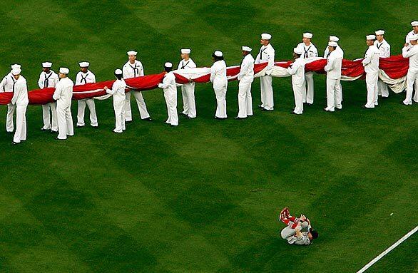 A Cardinals player finishes warming up as sailors prepare to unfurl a huge American flag before the start of Game 1 of the National League Division Series on Wednesday at Dodger Stadium.