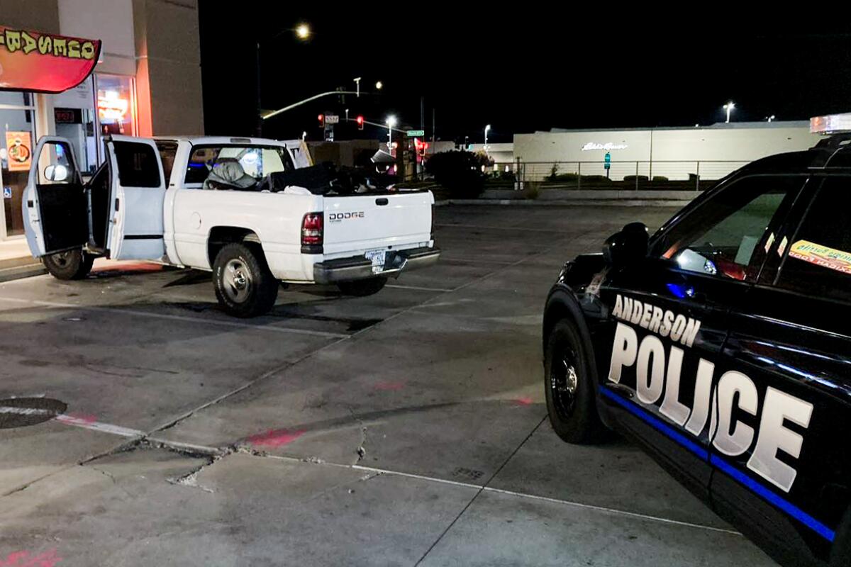 A white truck with its left-side doors open is shown in front of a police vehicle. 