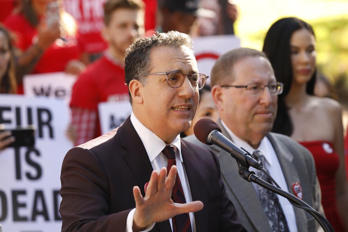 Two men in suits and glasses, one speaking into a microphone, before a crowd of animals rights activists.