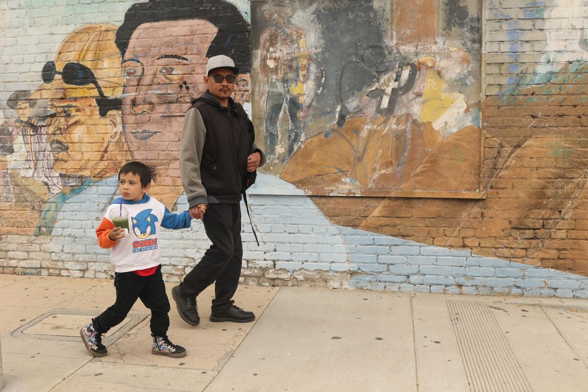 A father and his son walk pass a historic mural in central Anaheim where voters declined to recall their council rep.