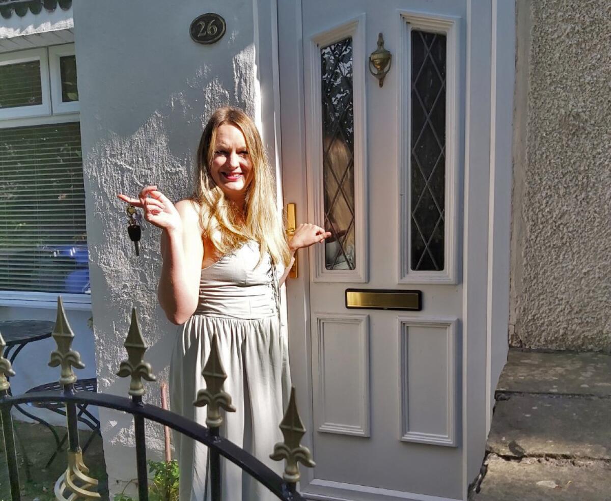 A woman standing between a front door of a home and its gate