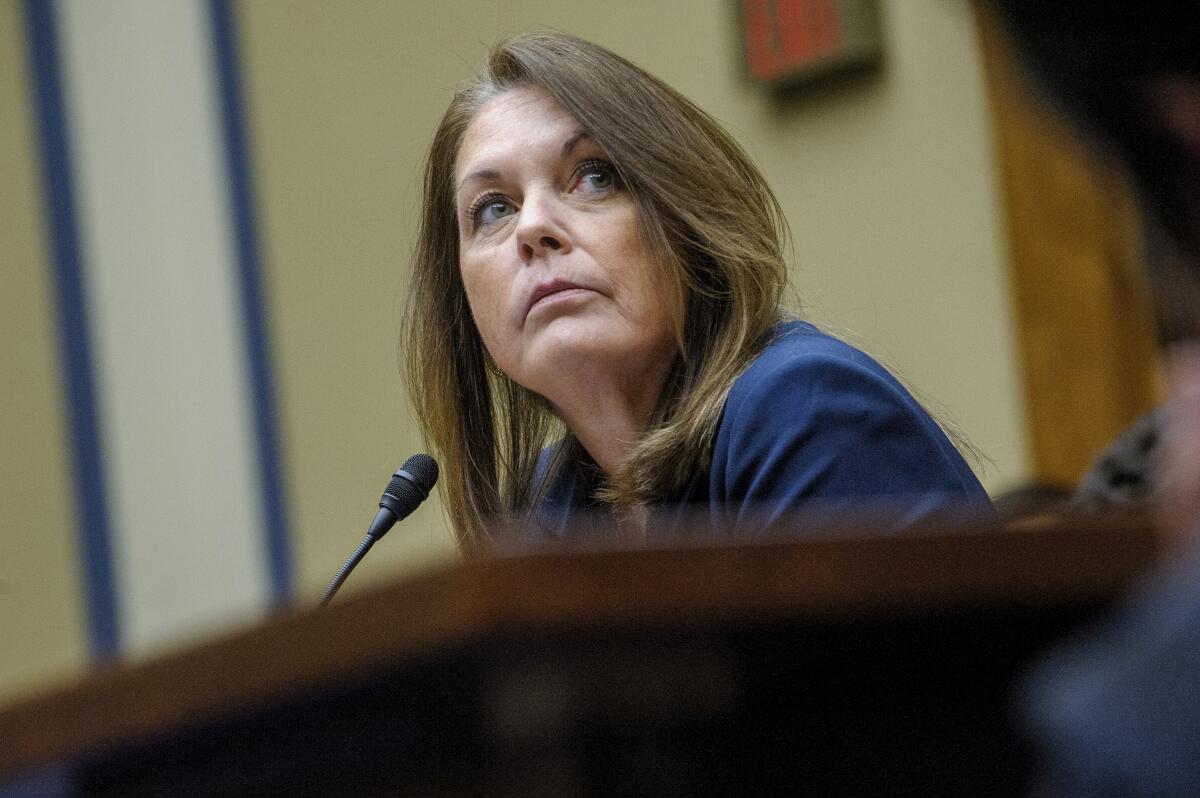 Kimberly Cheatle sitting at a table with a small microphone, looking up