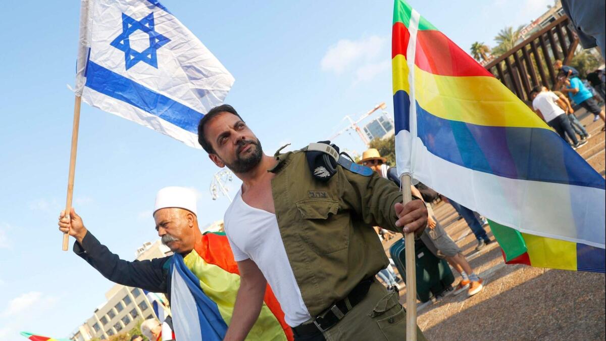 A Druze and Israeli veteran carry Israel and Druze flags. The Israeli veteran also wears an outfit that combines civilian clothes with a military uniform.