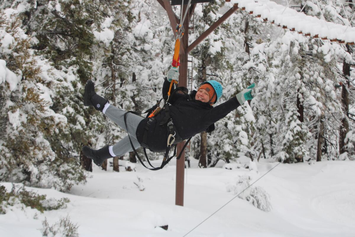 A smiling person suspended by a zipline against a snowy forest background.