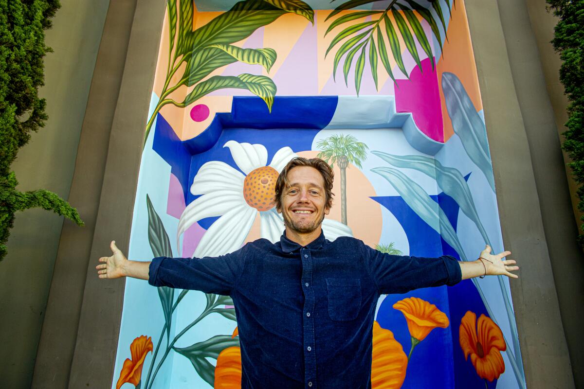 Artist Aaron Glasson poses in front of the new "Costa Mesa Bloom" mural he painted at the city's Triangle Square. The mural was officially dedicated Wednesday.
