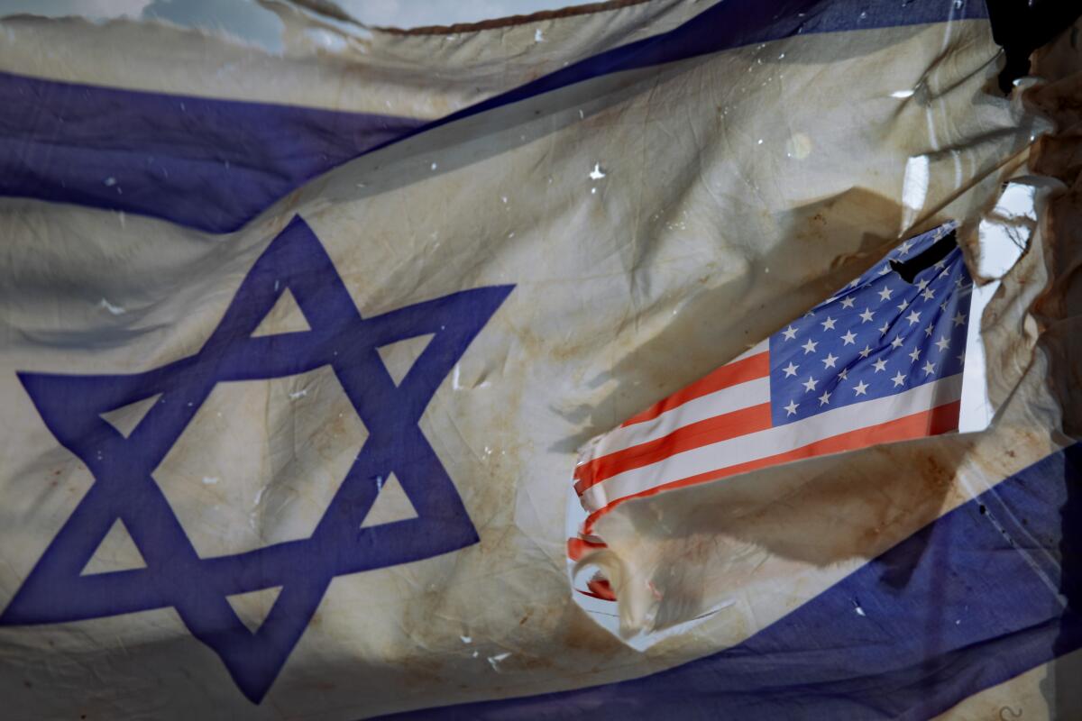 A U.S. flag is seen through a hole torn in an Israel national flag.