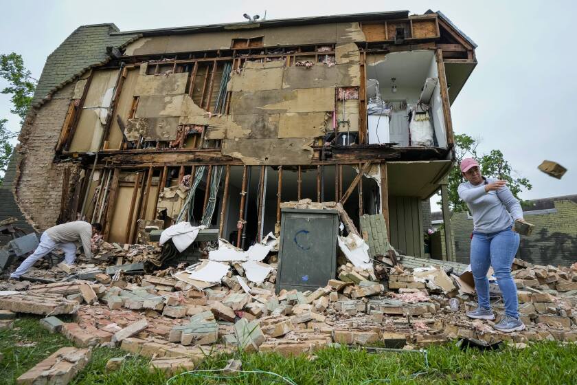 David Figueroa, left, and Delmy Suazo toss bricks to a pile as they work to clean up debris after a wall came down at an apartment complex in the aftermath of a severe storm on Friday, May 17, 2024 in Houston. Fast-moving thunderstorms pummeled southeastern Texas for the second time this month, killing at least four people, blowing out windows in high-rise buildings, downing trees and knocking out power to more than 900,000 homes and businesses in the Houston area. (Brett Coomer/Houston Chronicle via AP)