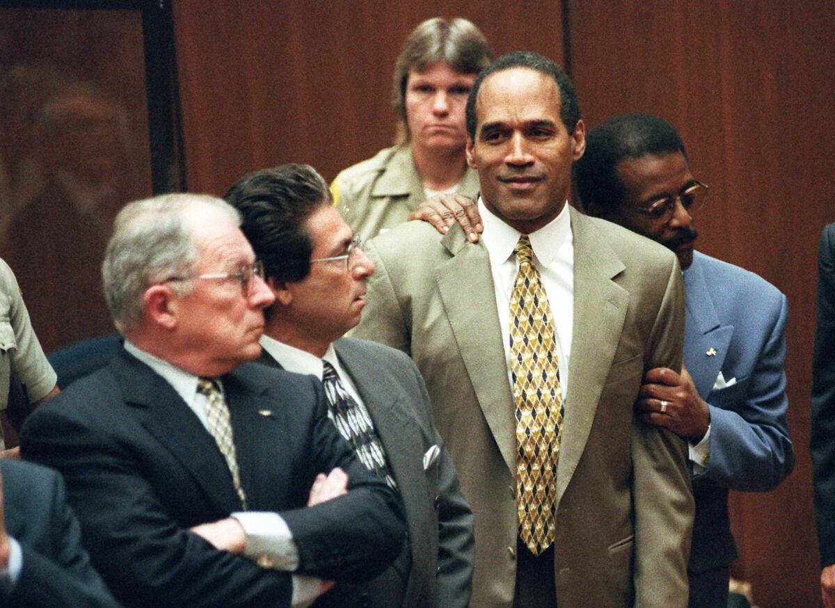 O.J. Simpson smiles as Johnnie Cochran holds him from behind while F. Lee Bailey and Robert Kardashian stand by