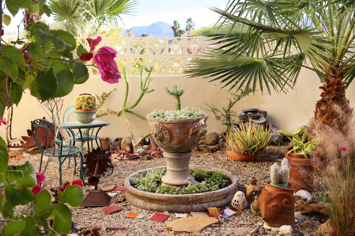 A walled garden at a desert home has a fountain filled with succulents, garden art, a table and chairs and various plants.