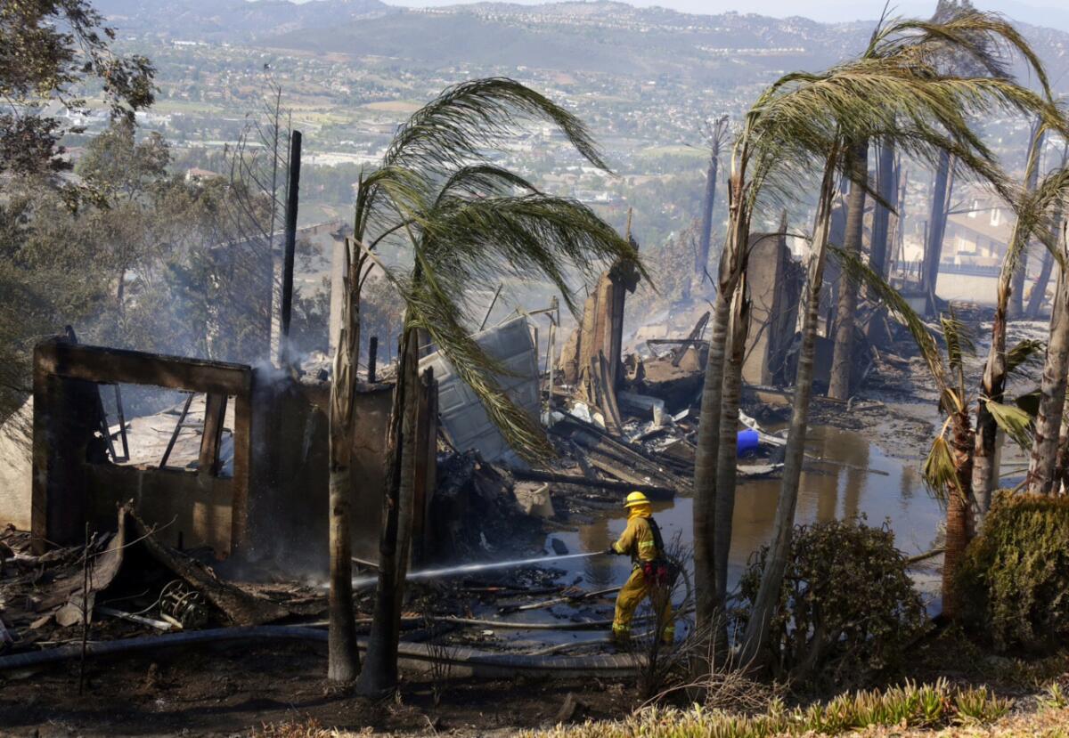 A firefighter puts out hot spots at a burned home in San Marcos.