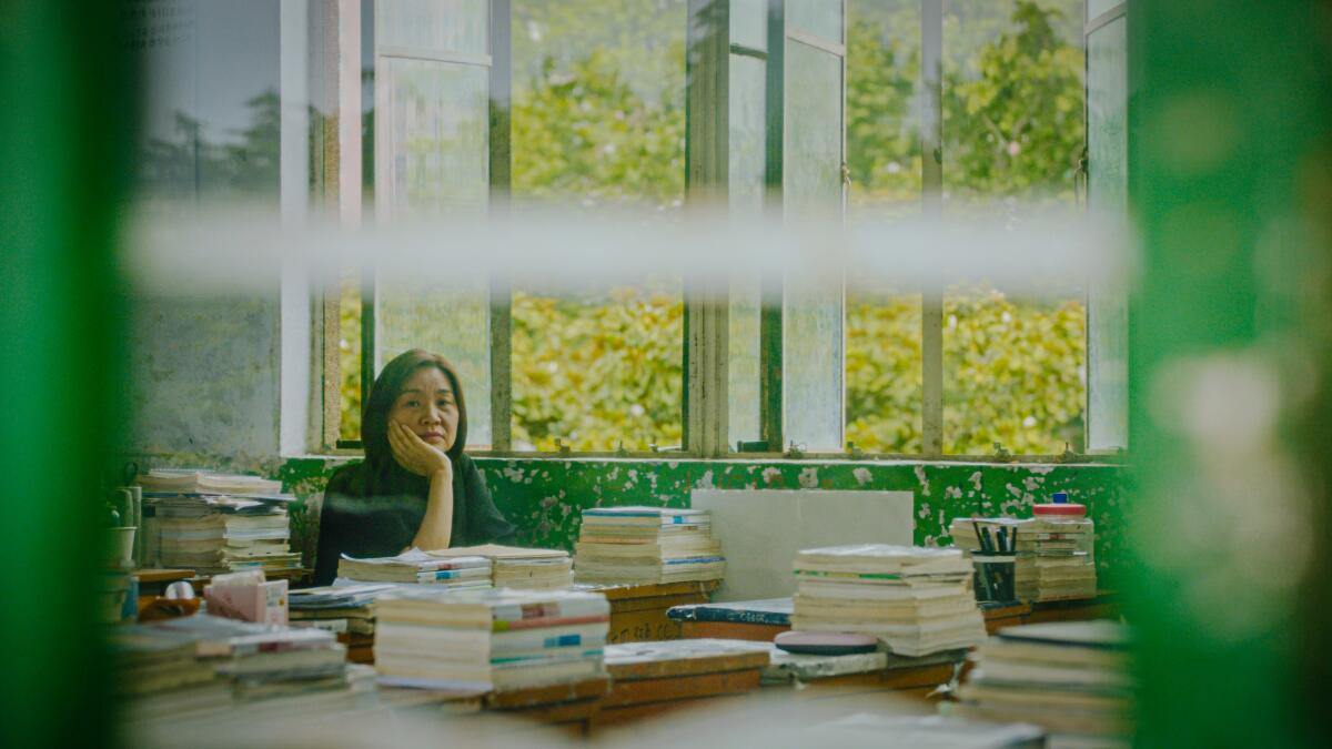 Author Liang Hong sits behind tables stacked with books.