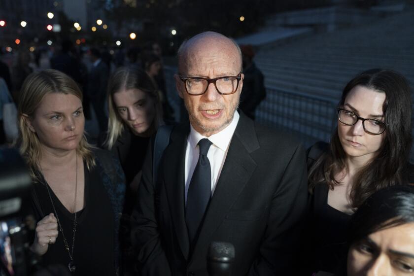 An older man speaks to an off-camera reporter outside a courthouse, flanked by three younger women