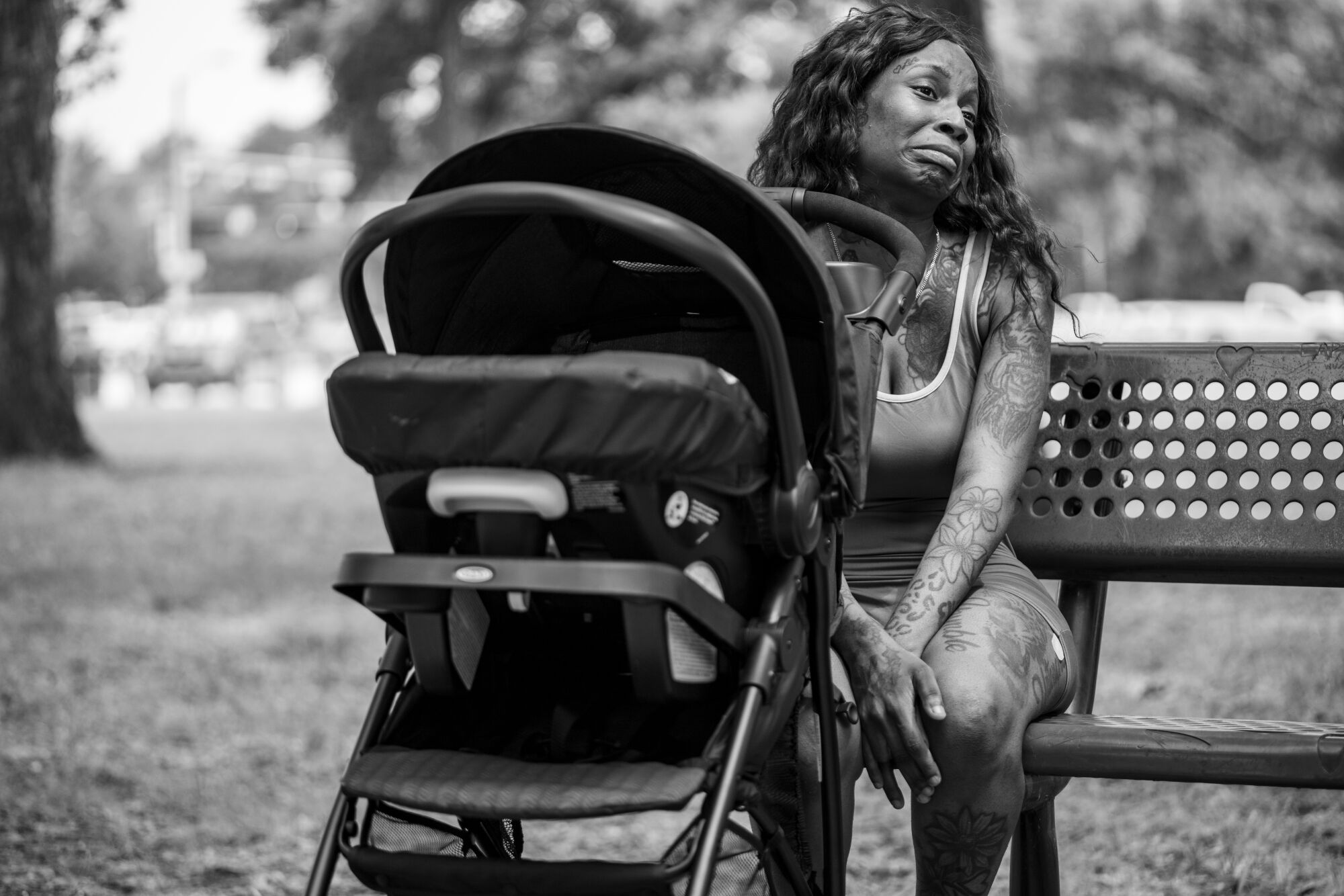 A woman sits on a park bench next to a stroller 