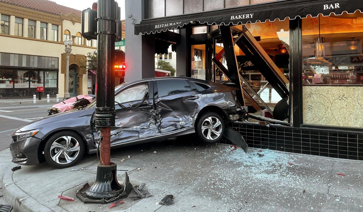 A banged-up car sits with its rear inside the restaurant storefront and its front facing the street