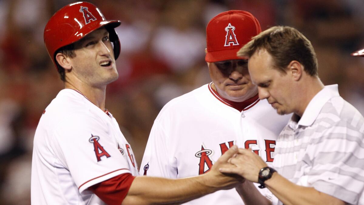 Angels third baseman David Freese, left, is examined by team trainer Adam Nevala, right, with manager Mike Scioscia, center, looking on during the third inning of Friday's game against the Texas Rangers.
