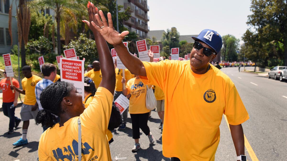 Gerald Gates, a worker at Pavilions market in Burbank, high-fives union representative Samantha Christian as they march with grocery workers and supporters on Aug. 2 through Los Angeles to demand a new contract.