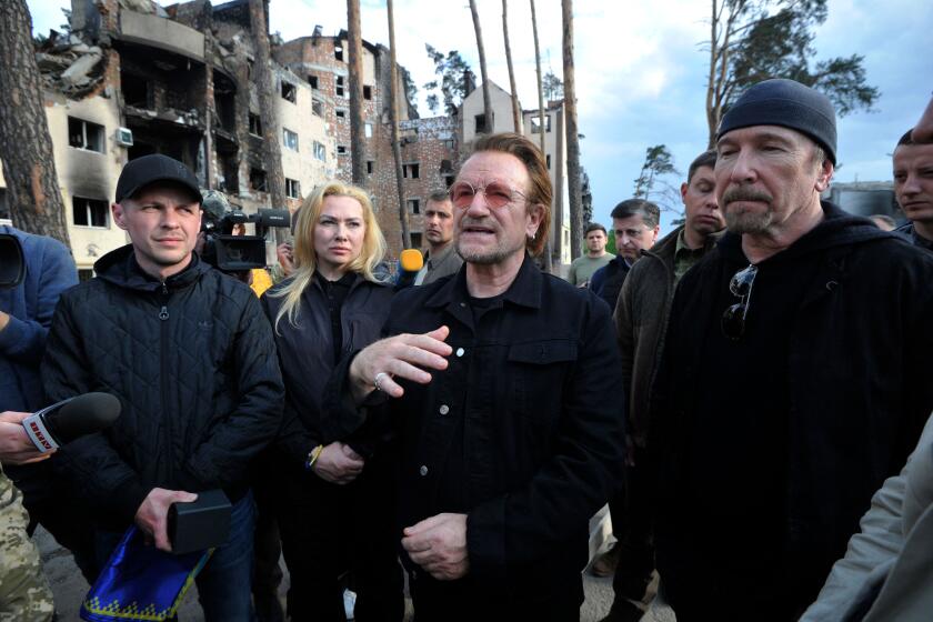 Bono (C) (Paul David Hewson), activist and front man of the Irish rock band U2 (C) and and guitarist David Howell Evans aka 'The Edge' (R) greets people as they inspect the damage to a residential area in the Ukrainian town of Irpin, near Kyiv on May 8, 2022. (Photo by Sergei CHUZAVKOV / AFP) (Photo by SERGEI CHUZAVKOV/AFP via Getty Images)
