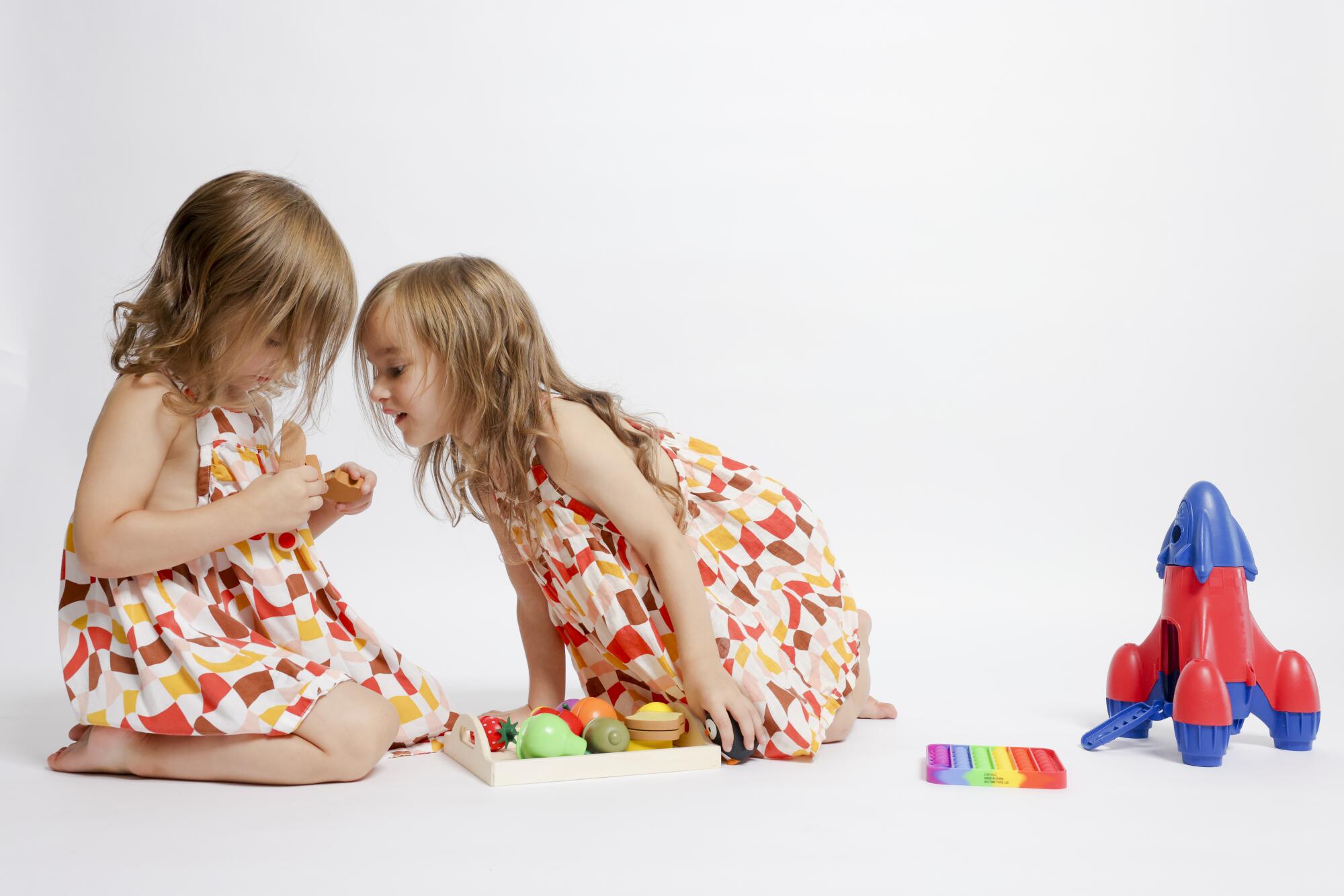 River and Penny Atchison, left and right, play with wooden and plastic toys at their home.