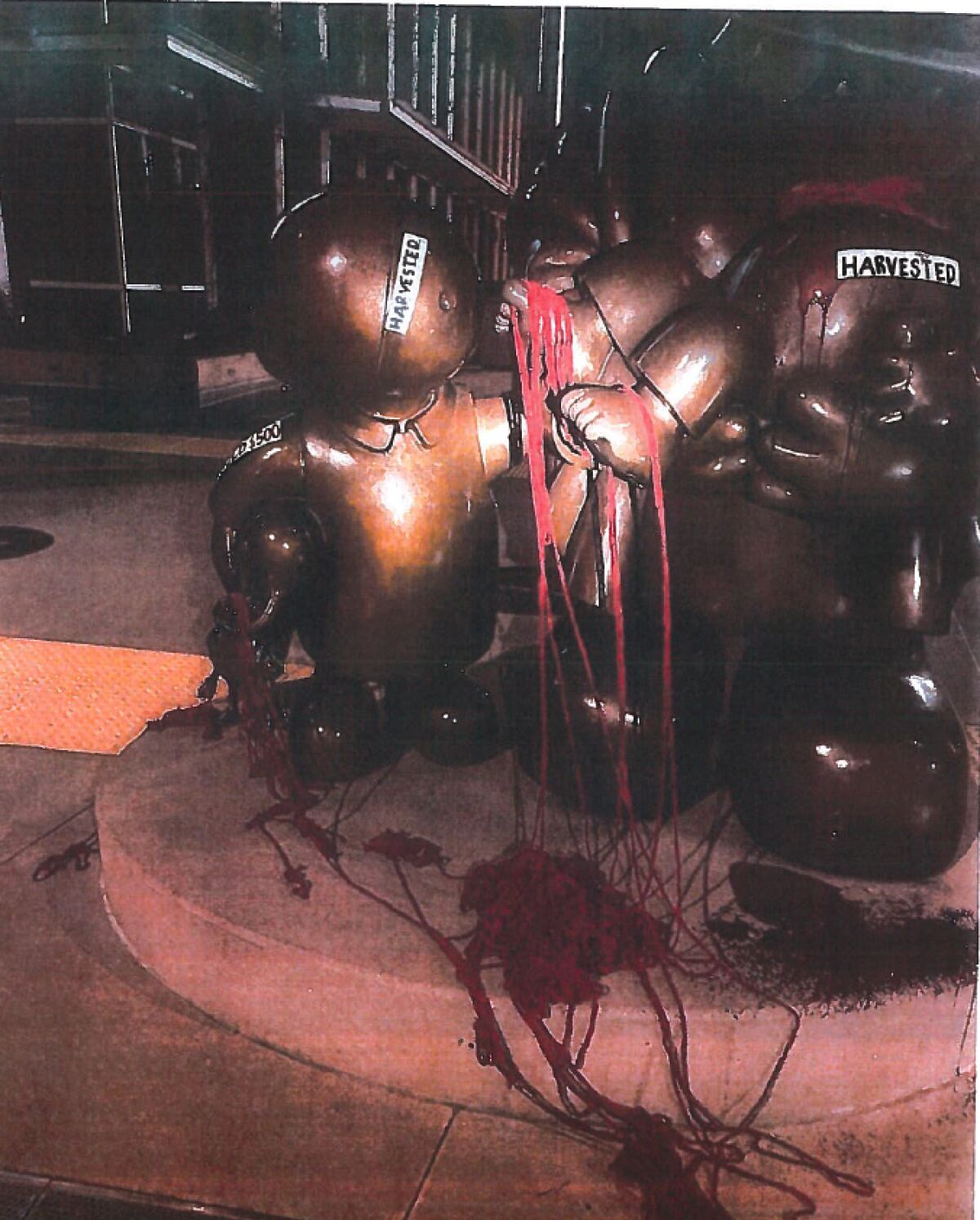 A statue defaced with fake blood and stickers that say "harvested"
