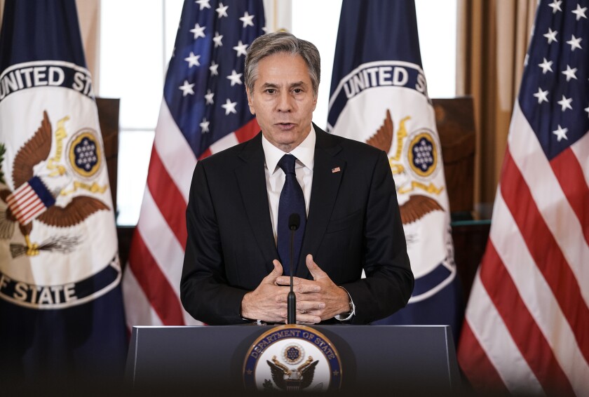 Secretary of State Antony J. Blinken speaks in front of a display of U.S. and State Department flags. 