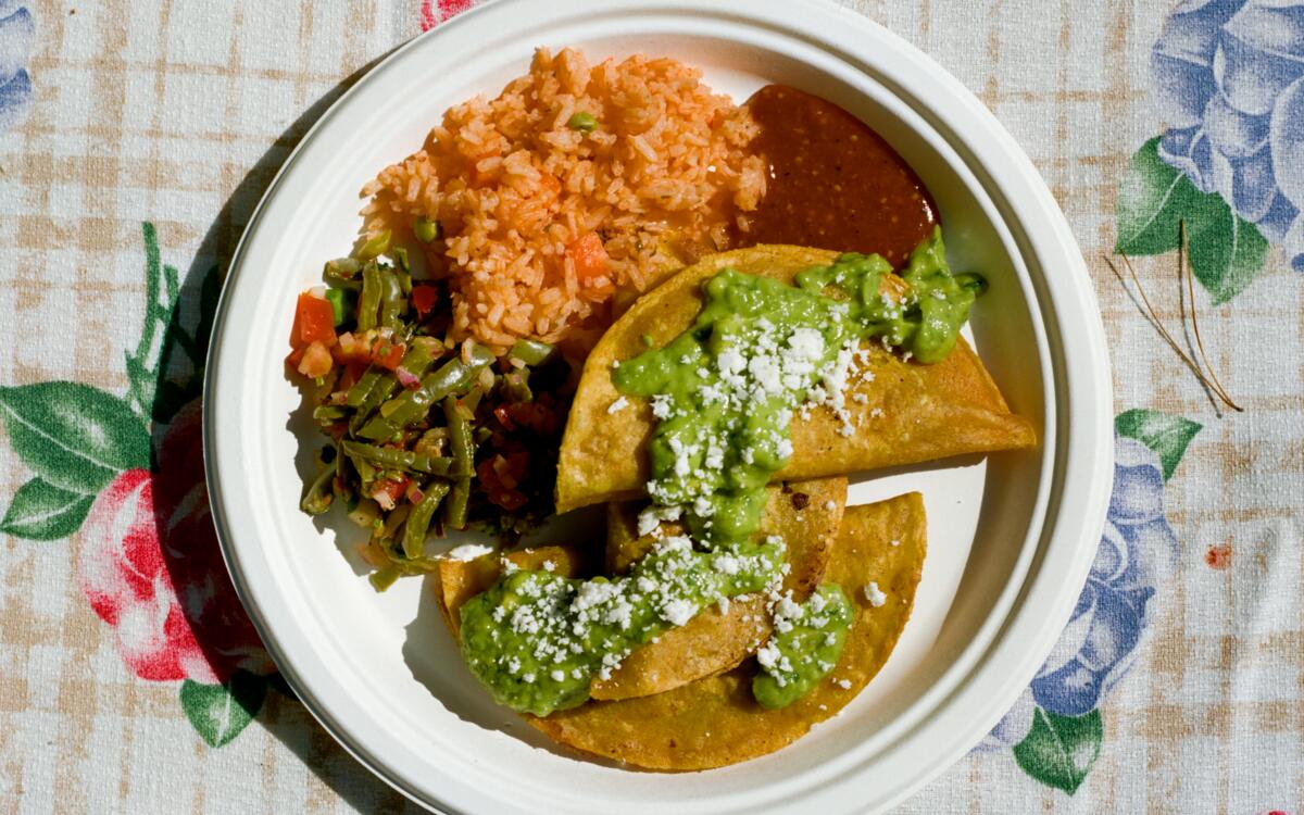 A plate of tacos, topped with guacamole and cheese, with sides of rice, poblanos and salsa.