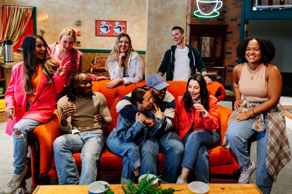 A group of people sit on an orange couch in a cafe.