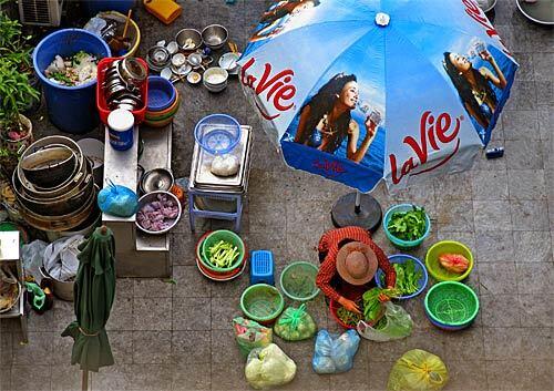 Hanoi, the capital city of Vietnam, still has traces of French influence after the 100-year occupation, which ended in 1950. A woman prepares food on a rooftop under an umbrella advertising LaVie water from France.
