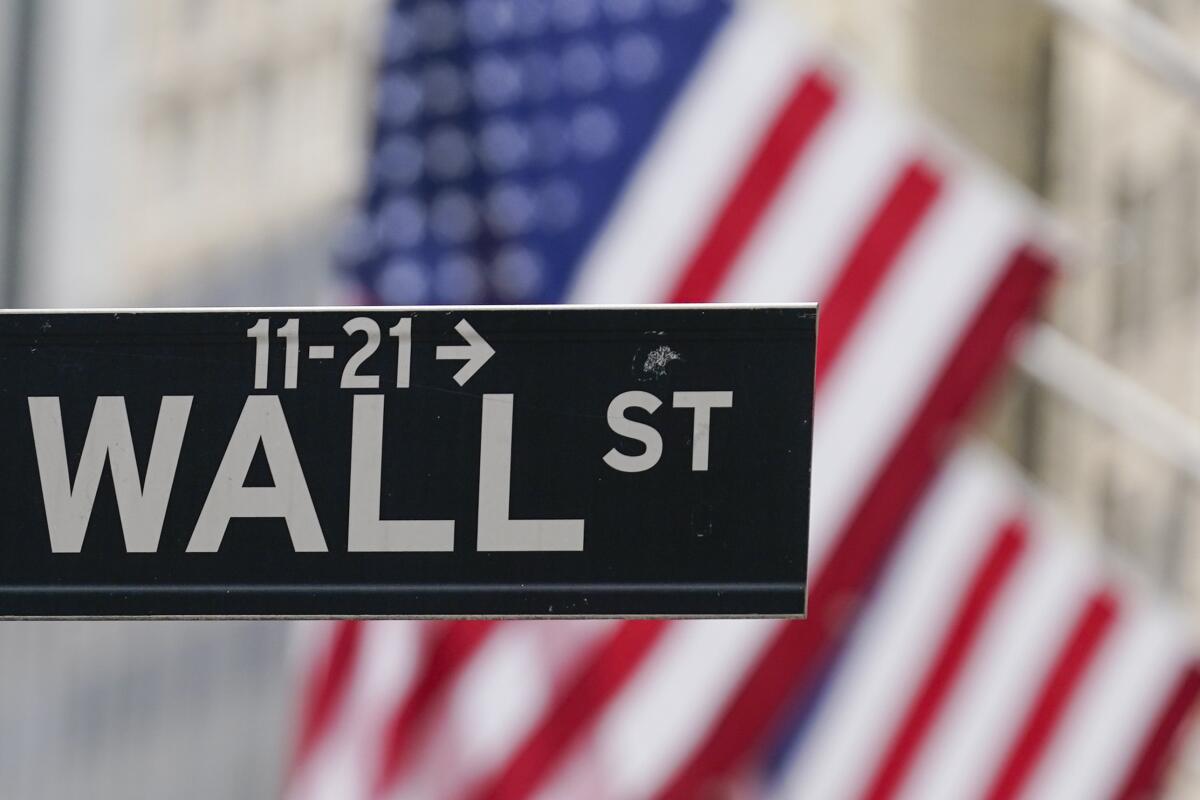A Wall Street sign hangs in front of an American flag in New York.