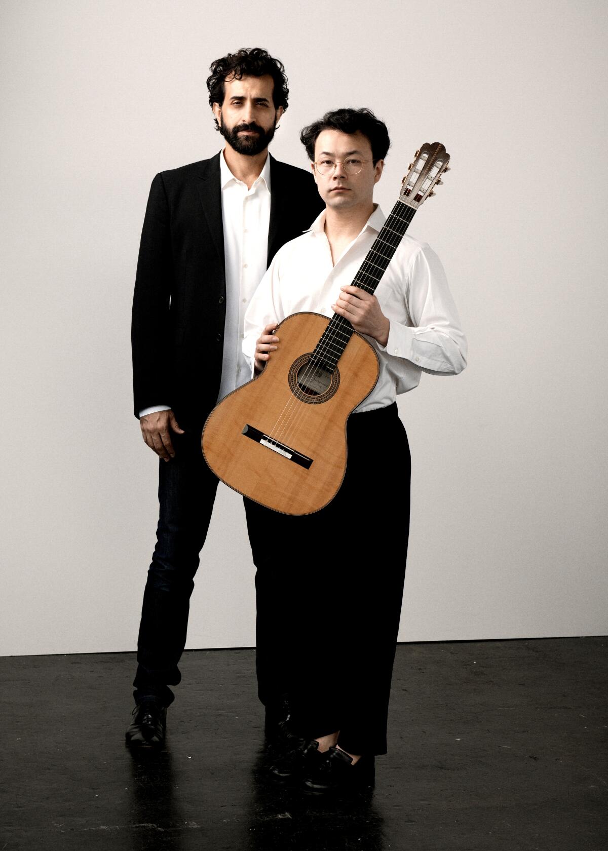 A man with a guitar standing in front of another man.