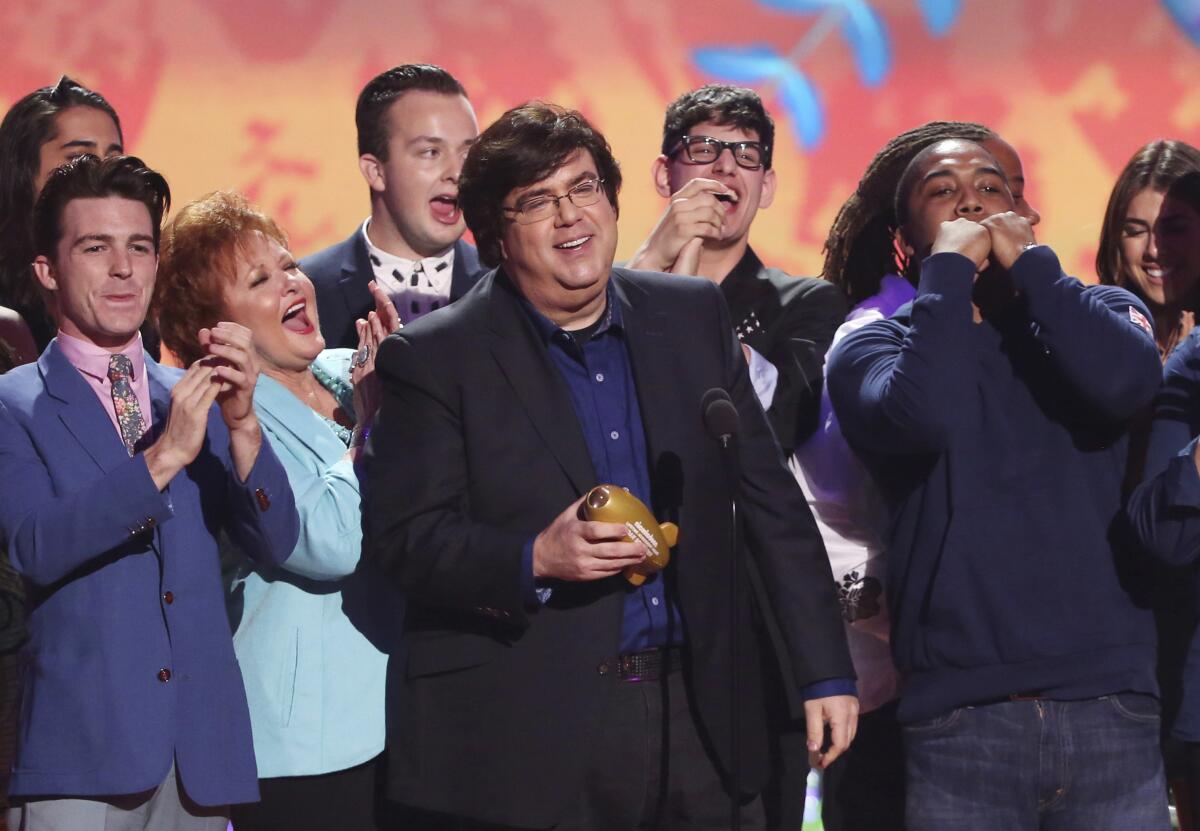 Dan Schneider holds an award onstage while a group of people cheer around him