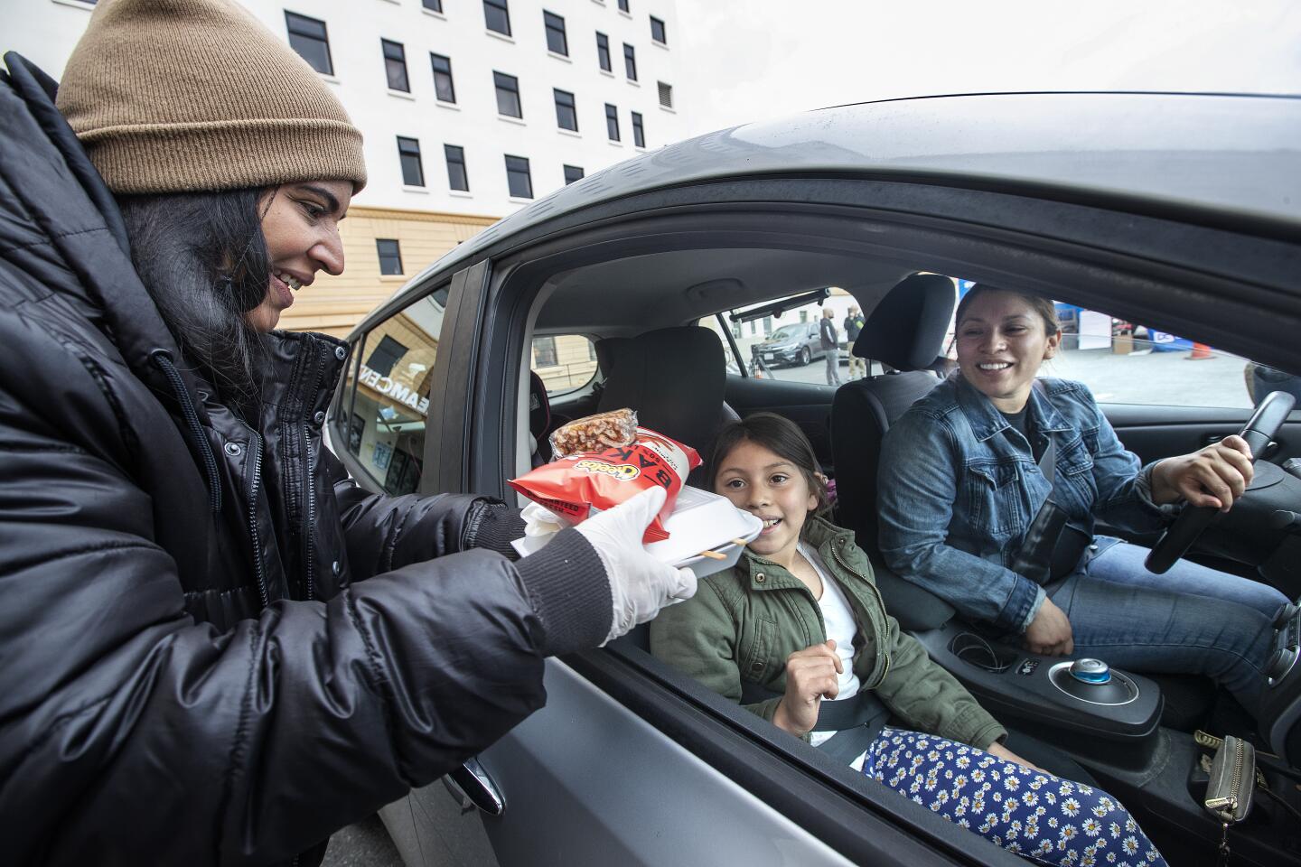 Volunteer Rachel Figueroa, serves a free lunch to go to Destiny Mendez, with her mother, Estefany, at the Dream Center in Los Angeles. LAUSD students can get free breakfast, lunch and dinner at the Dream Center, Monday through Friday.