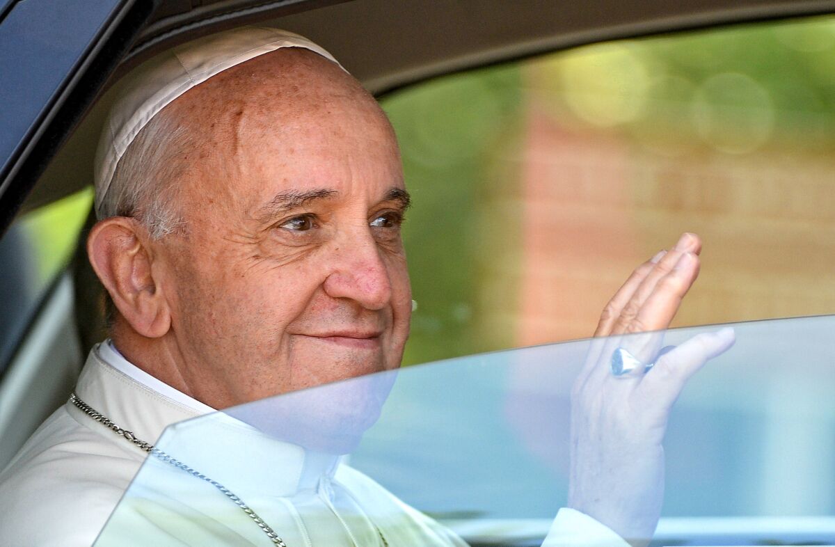The pope waves from inside a car.