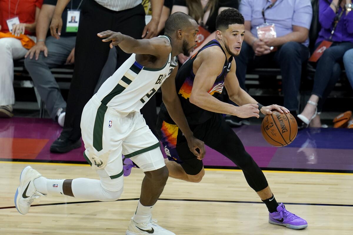 Phoenix Suns guard Devin Booker, right, dribbles against Milwaukee Bucks forward Khris Middleton during the second half of Game 2 of basketball's NBA Finals, Thursday, July 8, 2021, in Phoenix. (AP Photo/Ross D. Franklin)