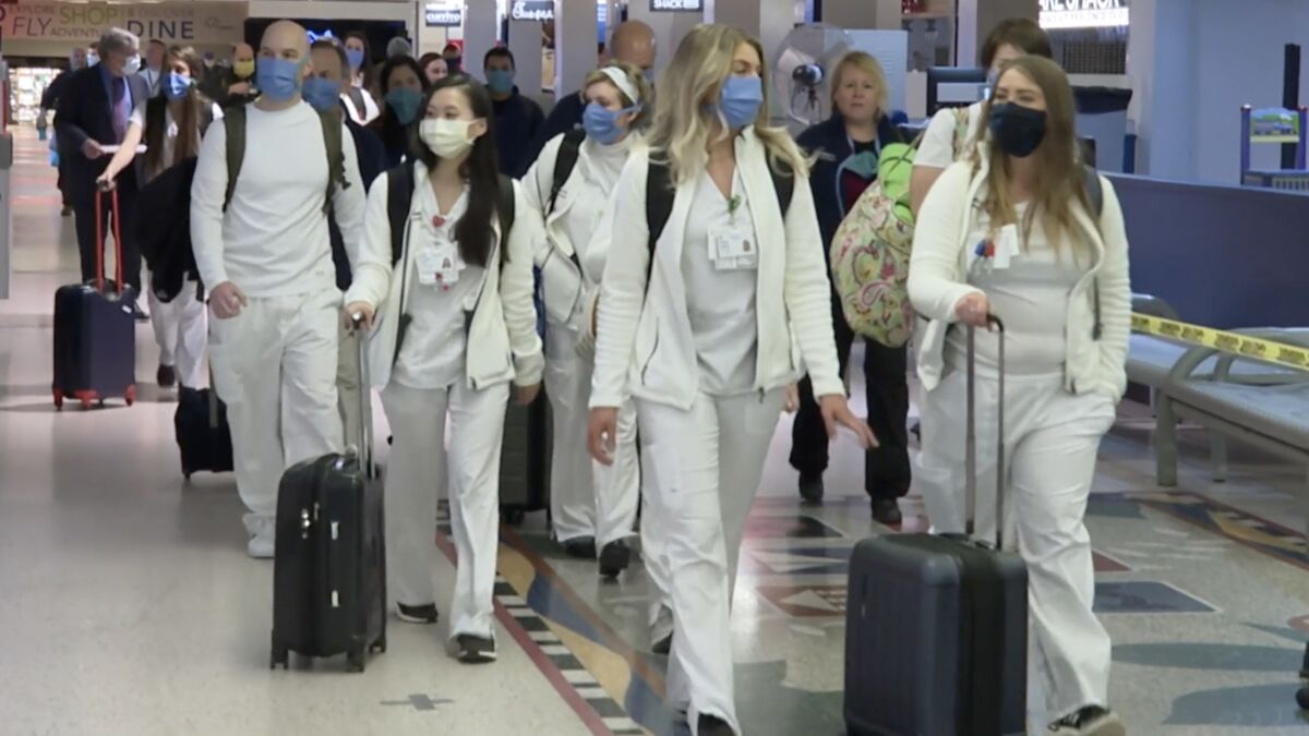 Medical workers in scrubs wheel suitcases through an airport in "Heroes on the Front Line."