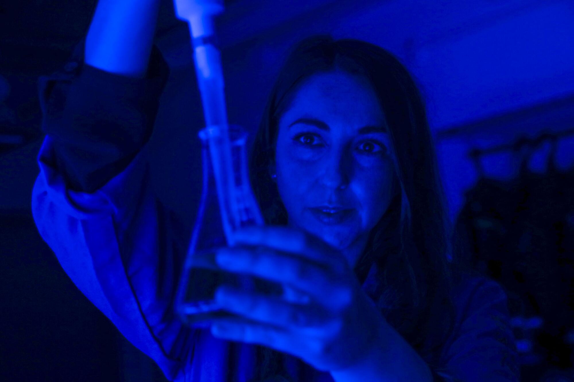 A woman bathed in blue light manipulates laboratory equipment