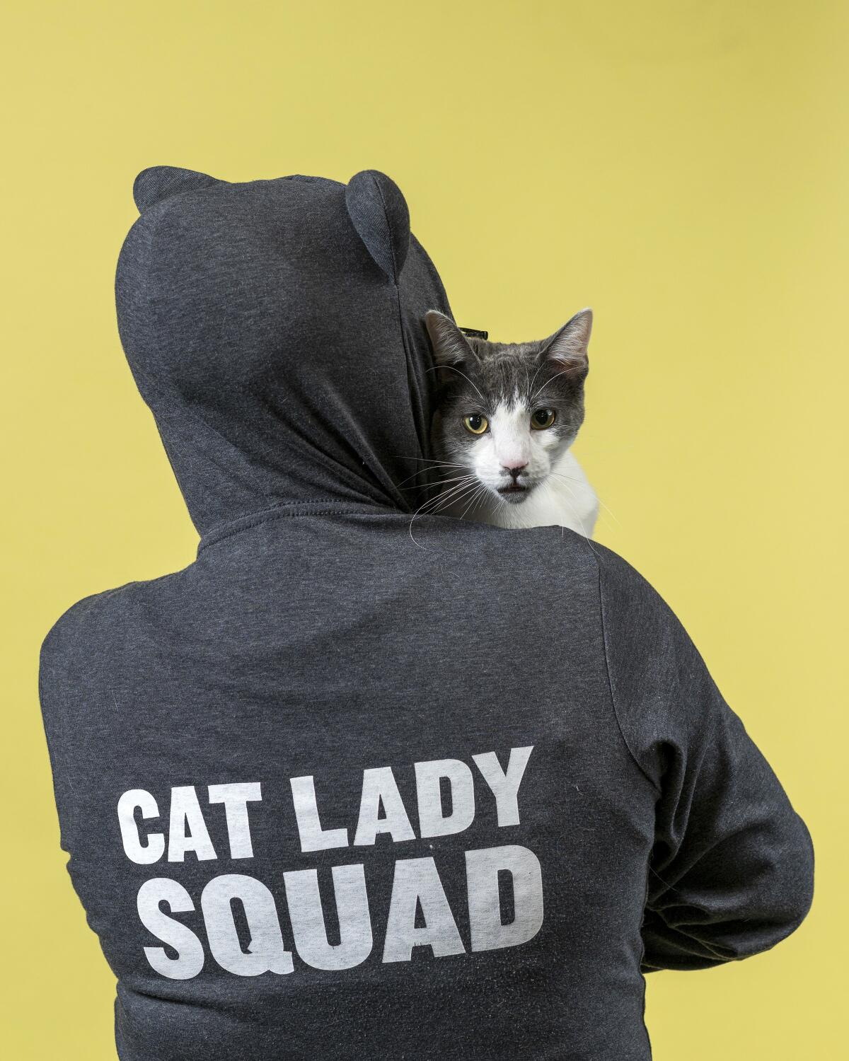 Stoffel the cat looks over the shoulder of Esther Su, who is wearing a hoodie that says "Cat Lady Squad."
