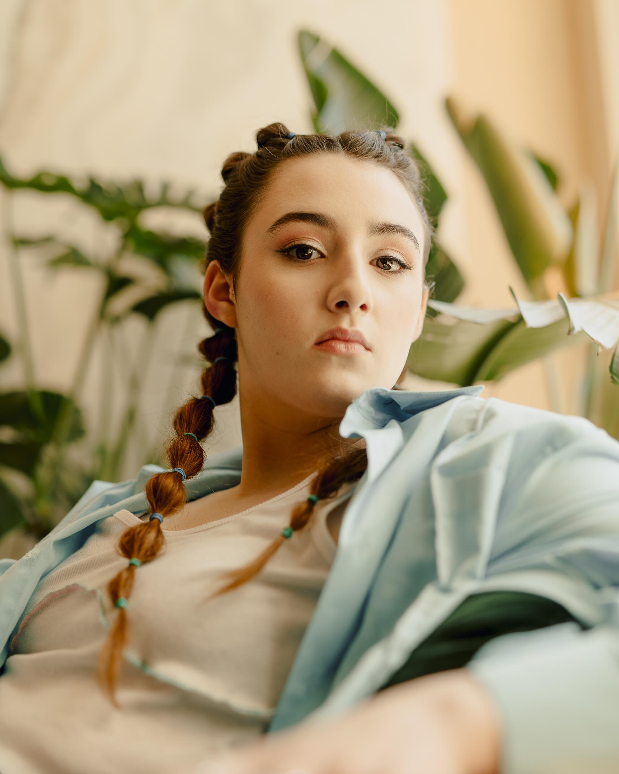 A young woman poses in front of a plant.