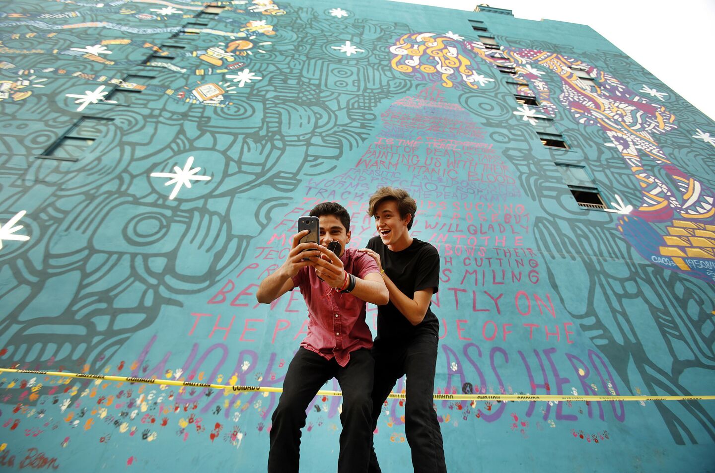 Tony Davia, left, takes a photo with Lucas Connor, both bandmates from Laguna Beach, in front of a mural on the Santa Fe Building at 539 S. Los Angeles Street in downtown L.A., created by the artist Young & Sick for the band Foster the People.
